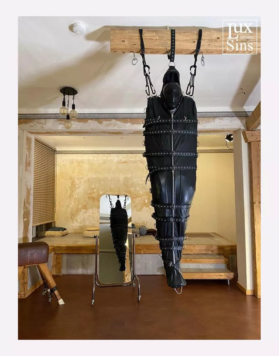 Suspended from tne ceiling in a leather sleepsack